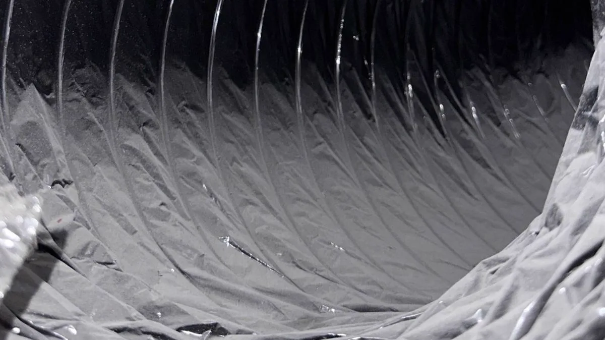 Dark flexible air duct with thick dust buildup before cleaning